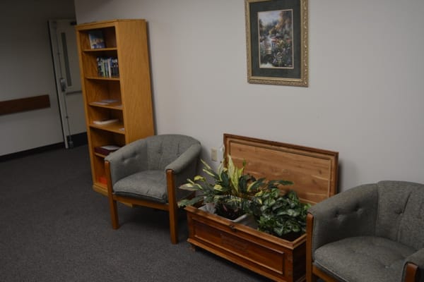 Two gray armchairs and a wooden chest with plants in a lobby