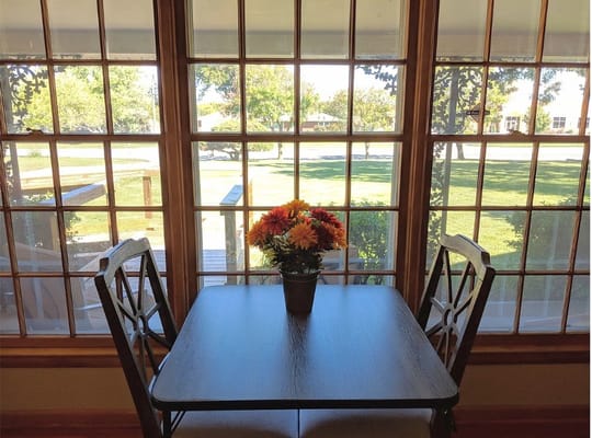 A table with a potted flower arrangement in front of large windows overlooking a green lawn.