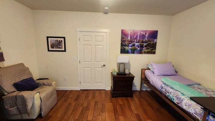 A cozy bedroom featuring a bed, chair, and artwork.