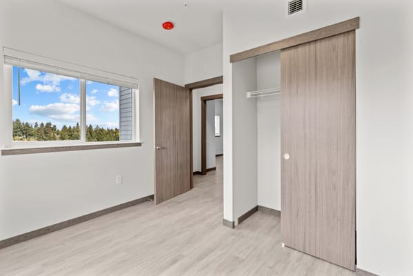 Light-filled bedroom with a sliding door and window overlooking greenery.