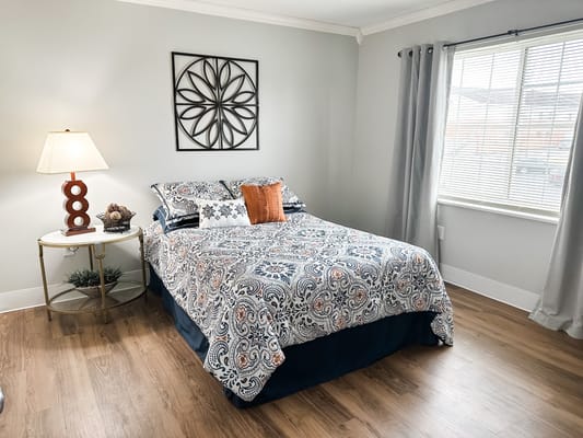 A neatly arranged bedroom with a patterned bedspread, lamp, and window.