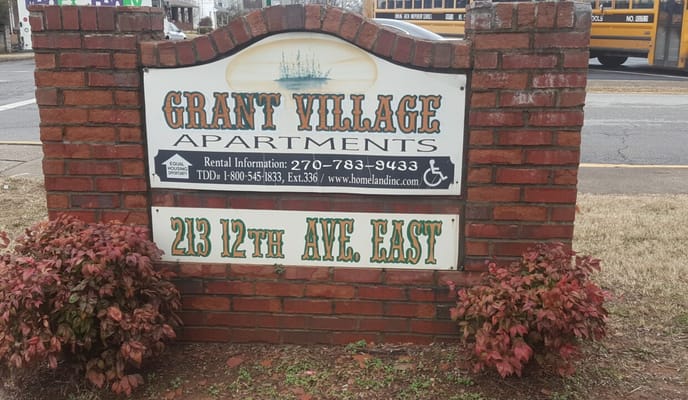 Sign for Grant Village Apartments displaying the address and contact information.