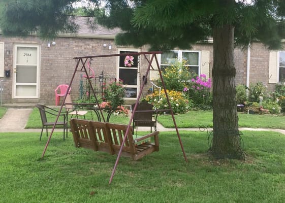 Wooden swing set in a garden area with flowers and chairs.