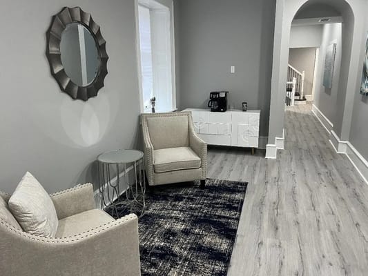 Elegant seating area with two armchairs, a round table, and a modern mirror.