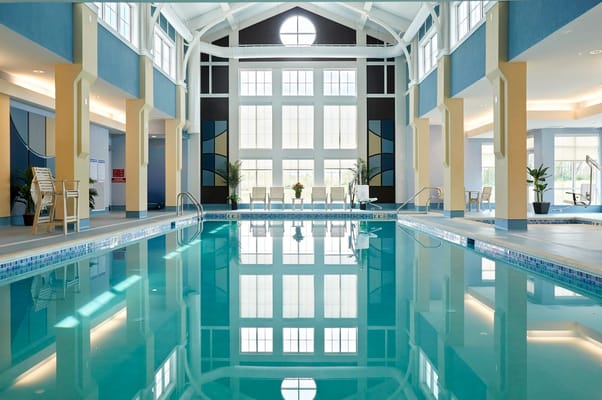 A serene indoor pool with lounge chairs and large windows.
