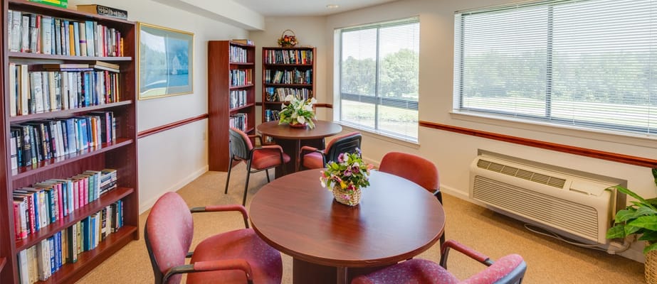 A reading room with bookshelves, two tables, and potted plants.