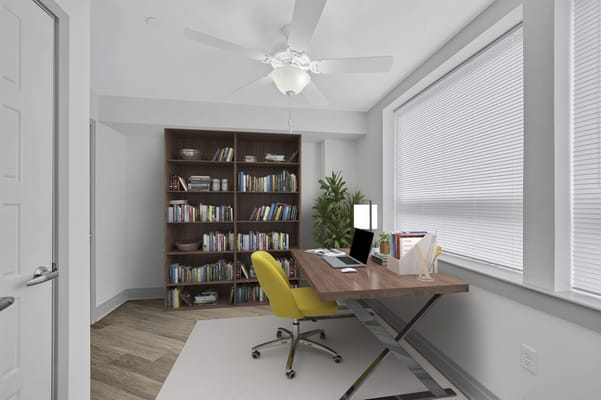 A bright office with a desk, yellow chair, and bookshelves.