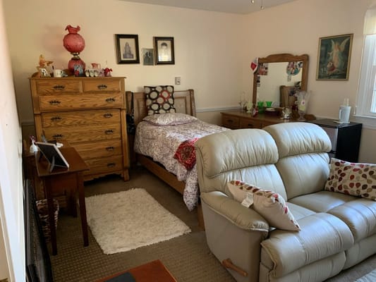 A well-decorated bedroom featuring a bed, dresser, and lounge chair.