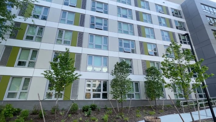 Modern apartment building with green accents and landscaping.