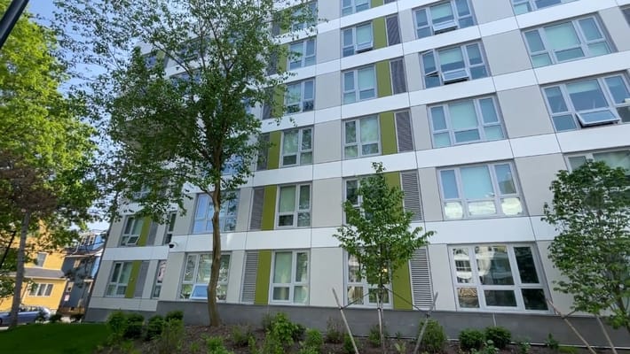 Modern apartment building with green accents and surrounding trees
