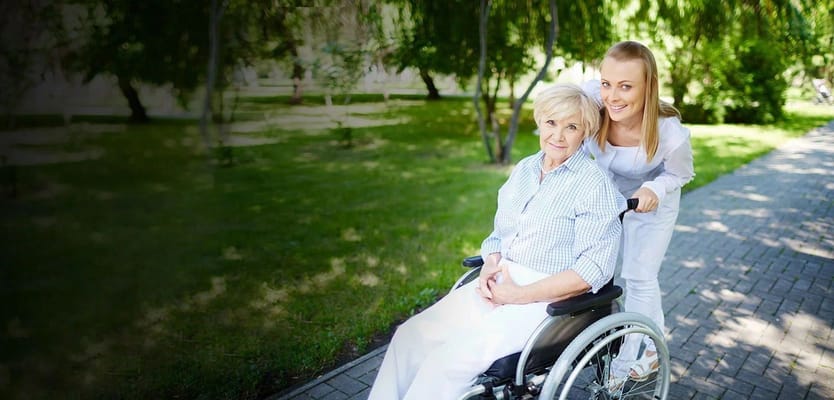 A caregiver assisting a resident in a wheelchair outdoors