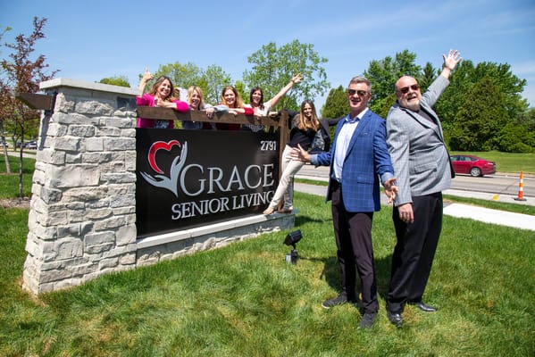 Staff and residents celebrating in front of Grace Senior Living sign