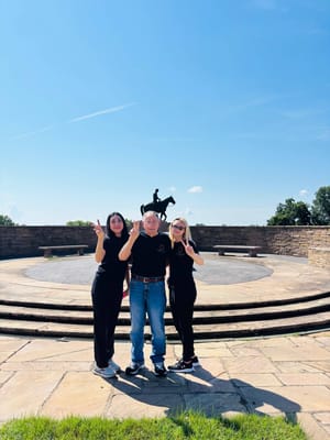 Three people posing outdoors with a statue behind them