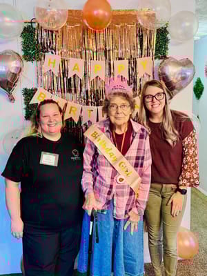 Residents celebrating a birthday with staff in a decorated common area