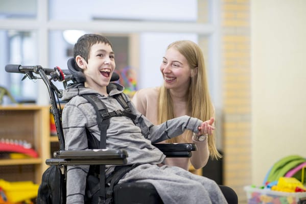 A young boy in a wheelchair laughing with a caregiver