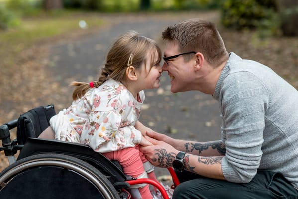 A playful moment between a girl in a wheelchair and a man outdoors