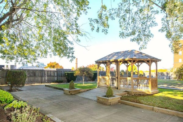 Wooden gazebo surrounded by greenery in a senior living facility garden.