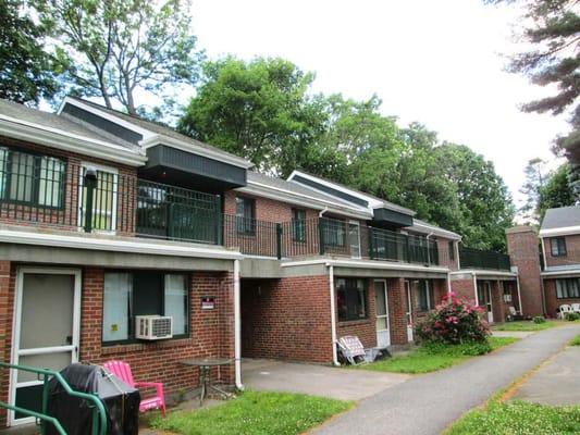 Two-story brick building with balconies and green surroundings at Norumbega Gardens.