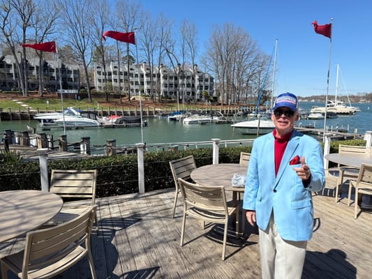 A man in a blue blazer standing on a deck overlooking a marina.