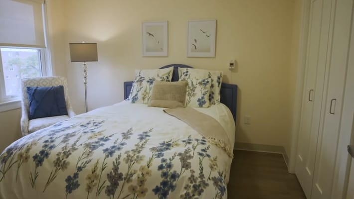 A bright bedroom featuring a bed with floral bedding and a chair.