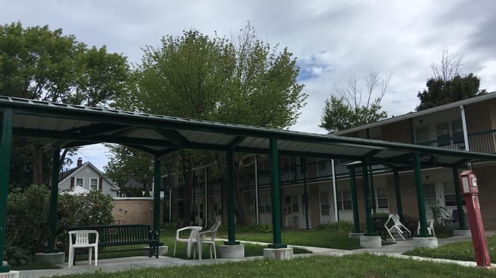 Covered outdoor seating area with green benches and chairs