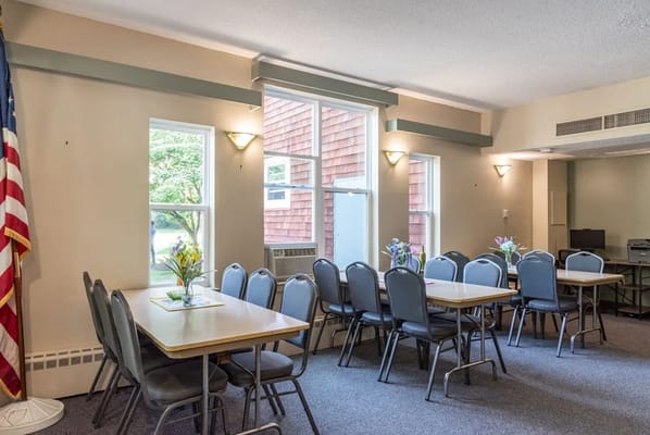 Common room with tables, chairs, and windows at Mill Pond Apartments