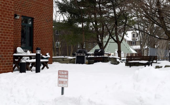 Snow-covered patio with benches and barbecue grill at Water Street Apartments.