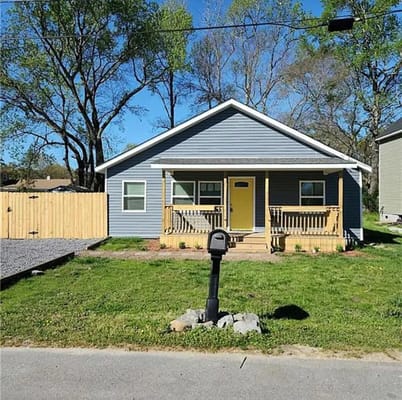 Blue house with a yellow door and porch, surrounded by grass and trees