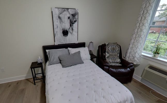 A cozy bedroom with a bed, a recliner chair, and a window.