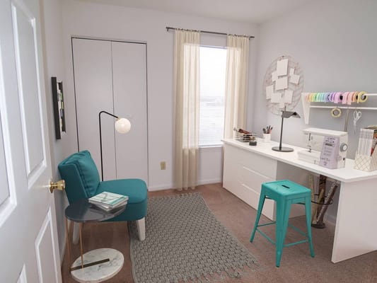 A study room with a teal chair, a small table, and a white desk featuring a sewing machine.