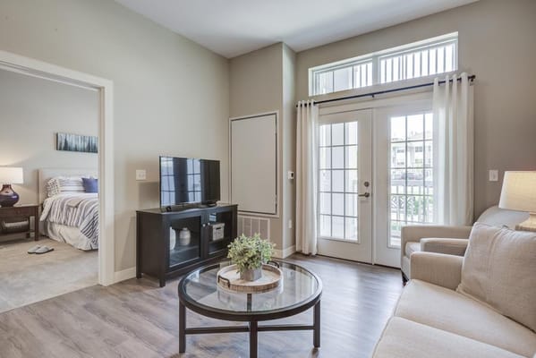 A spacious living room featuring a sofa, coffee table, and television with a view of a bedroom.