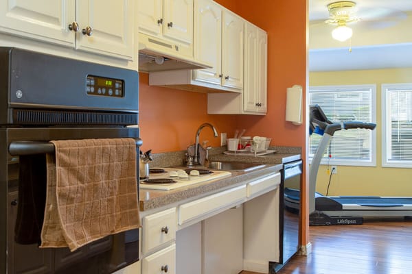 Modern kitchen with appliances and a treadmill in the next room.