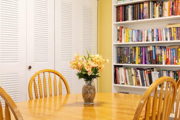 Wooden table with a vase of flowers in a room with a bookshelf