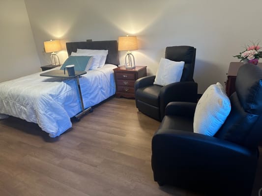 A cozy bedroom with a bed, two chairs, a bedside table, and lamps.