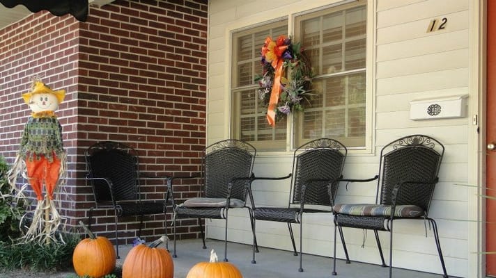 Porch with black chairs, pumpkins, and a scarecrow