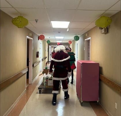 Santa Claus and an elf walking down a decorated hallway