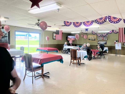 Seniors enjoying a festive gathering in the dining area decorated with balloons and flags
