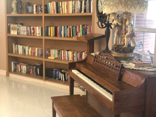 A wooden piano in a reading area with a bookshelf filled with books.