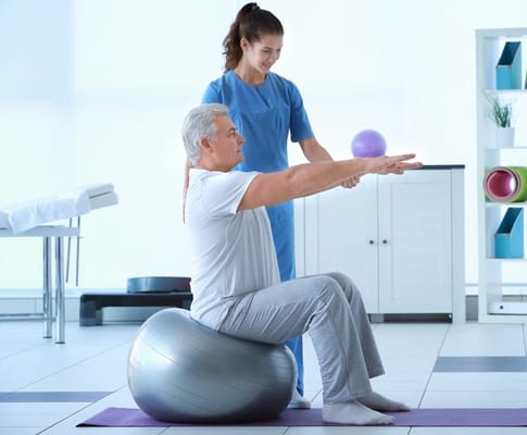 A senior exercising with staff assistance on a stability ball