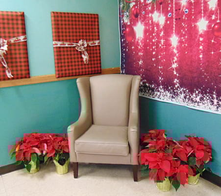 A beige armchair in a decorated corner with poinsettias and festive wall art.