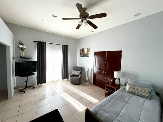 Well-lit bedroom with a bed, chair, and TV