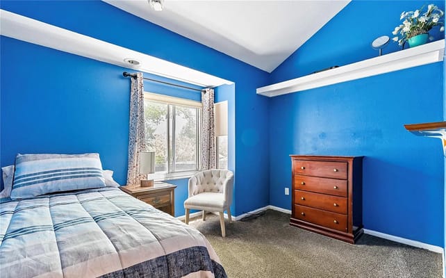 Bright blue bedroom with a bed, chair, and dresser