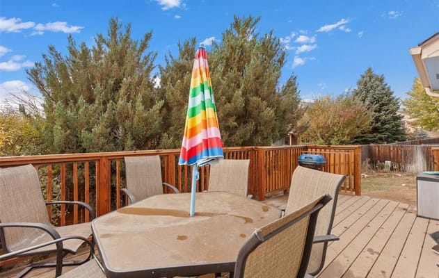 Table and chairs on a wooden deck with a colorful umbrella.