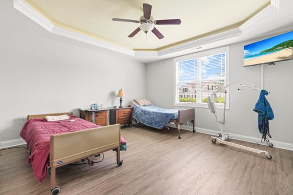 A cozy bedroom featuring two adjustable beds, a window with blinds, and a television.