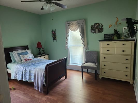 A neatly arranged bedroom with a bed, dresser, and chair.