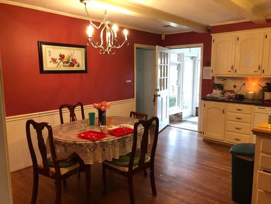 Dining room featuring a round table, flowers, and a kitchen area.