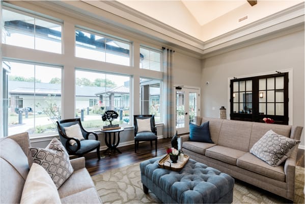 Cozy living room with large windows and comfortable seating at Grand Brook Memory Care.