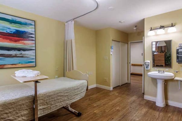 Patient room featuring a bed, artwork, and bathroom area.