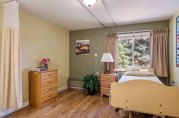 A cozy bedroom with a bed, dresser, lamp, and window view.
