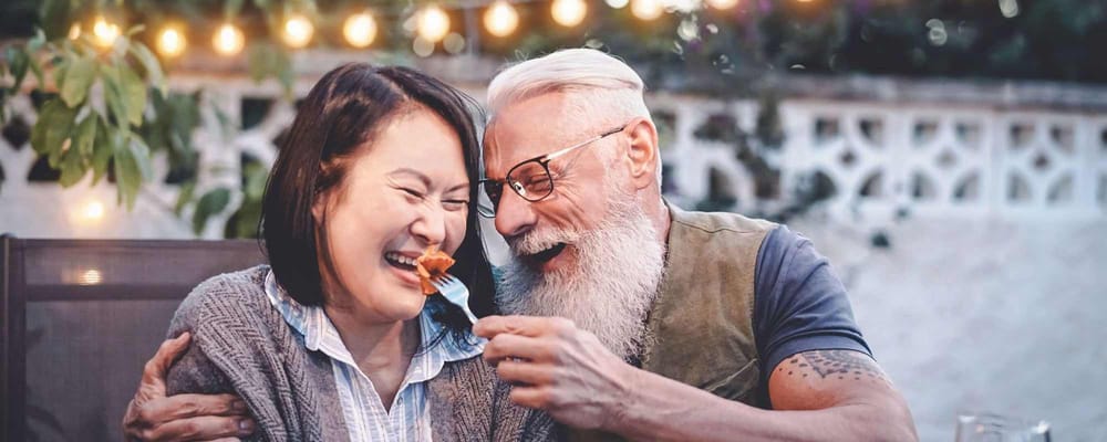 A man feeding a woman outdoors, both smiling